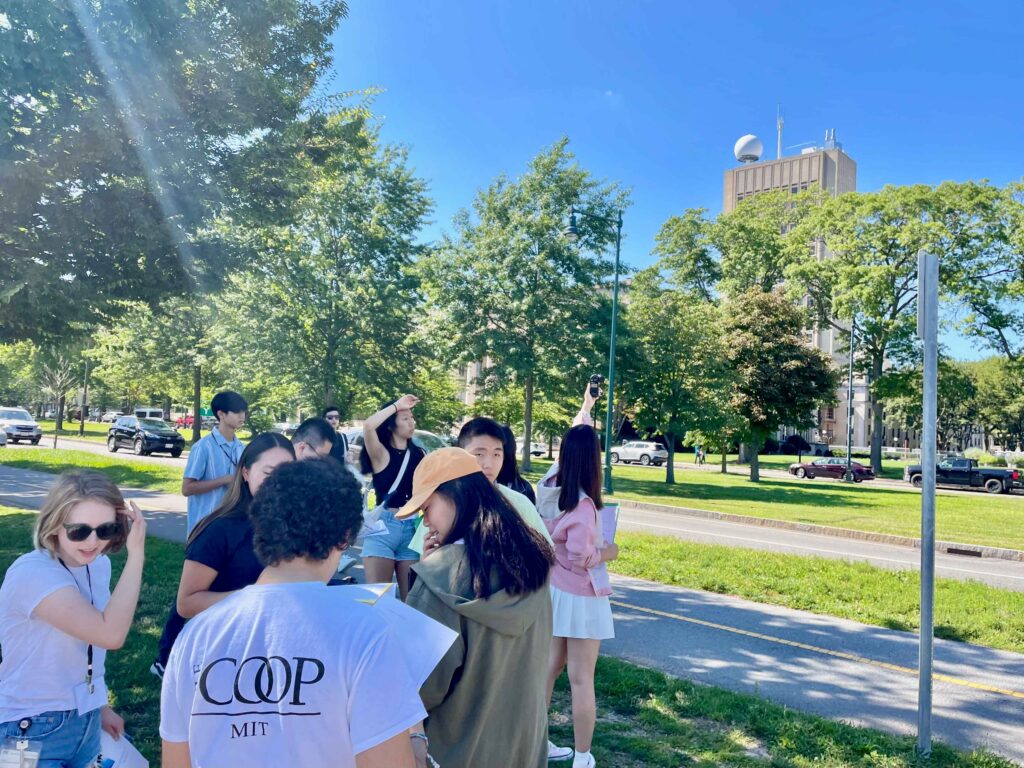 A group of students gather outside on a grassy lawn. In the background is the MIT Green building.