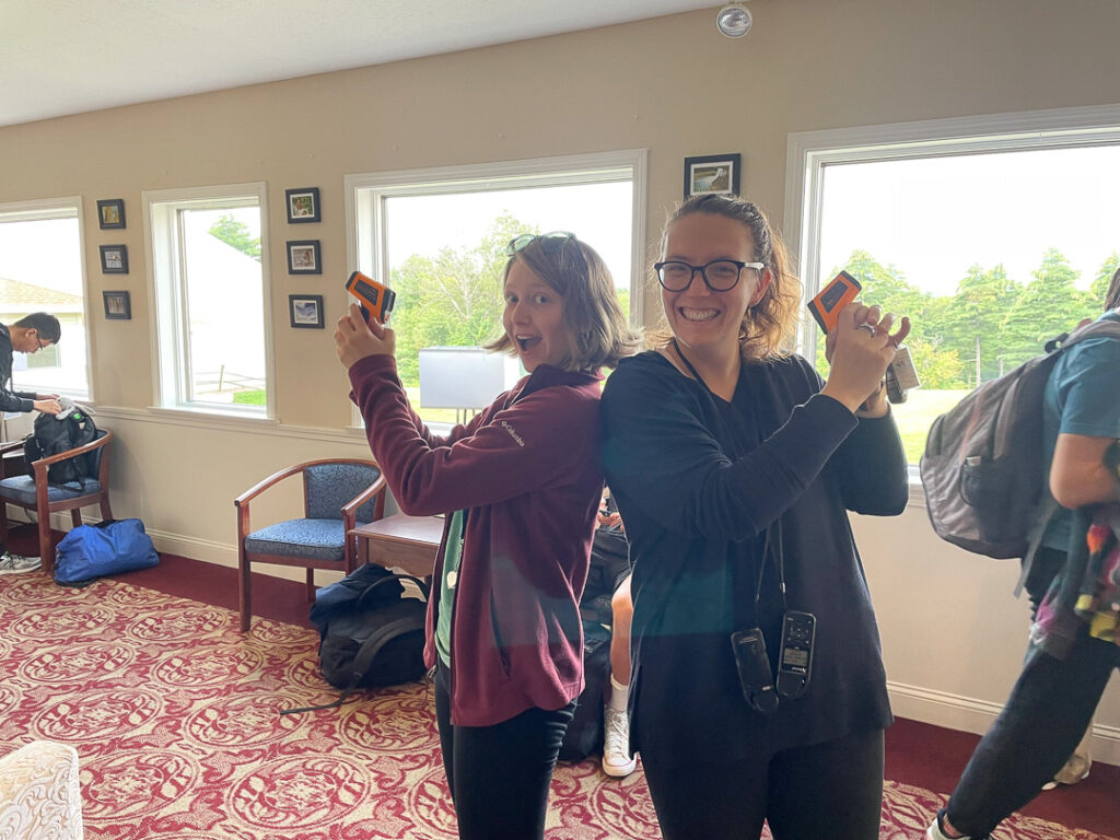 Grace O'Neil and Markey R Freudenburg-Puricelli stand back-to-back, posing with small scientific instruments like Charlie's Angels.