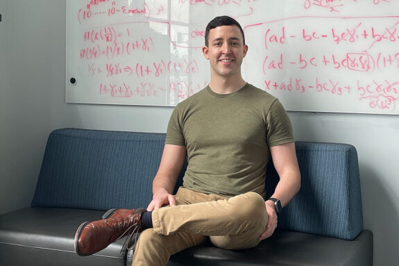 Justin Cole sits on a couch in front of a whiteboard of math equations.