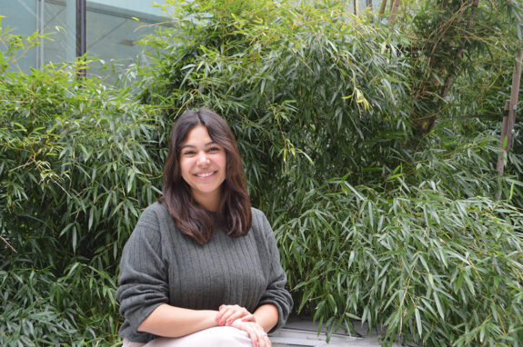 Lauren Aguilar sits on a bench and smiles at the camera, surrounded by bamboo.