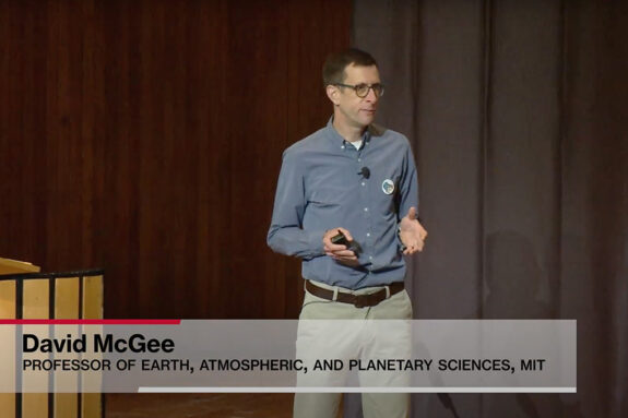 Still from a video of David McGee giving a talk on stage, holding a microphone.