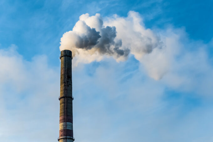 Industrial smokestack emitting smoke into a blue sky.